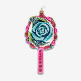 A decorative glass ornament shaped like a flower, featuring a blue and white swirl rose design on a white center, surrounded by pink glittery scalloped edges and a pink handle with red glitter dots, shown against a plain light gray background.