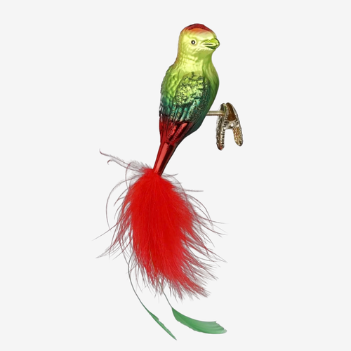 A decorative bird-shaped ornament or figurine with a green and red body, a bright red feather plume, and a small metallic perch, shown on a plain light gray background.
