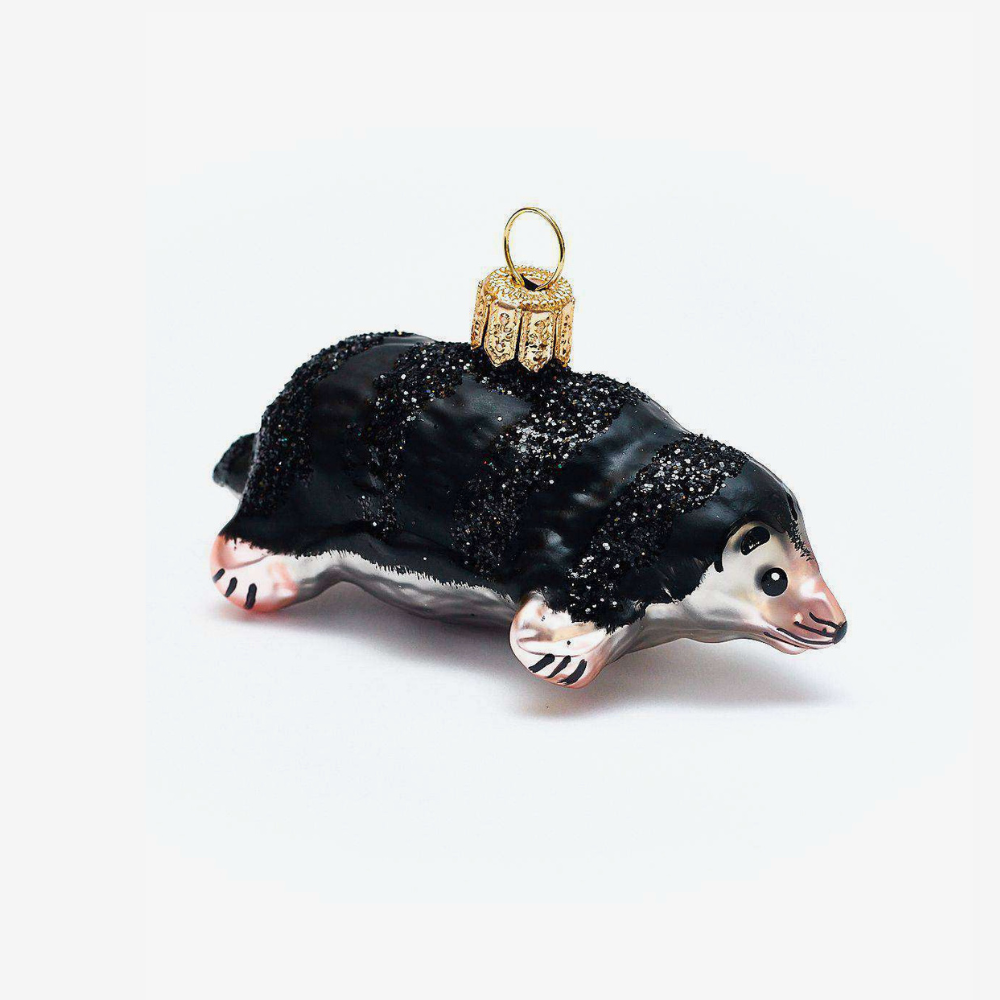 A small glass ornament shaped like a mole, with a glossy black body, pale pink and white face and paws, and a gold hanging loop at the top, photographed on a plain light background.