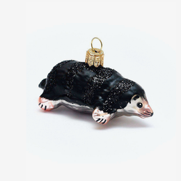 A small glass ornament shaped like a mole, with a glossy black body, pale pink and white face and paws, and a gold hanging loop at the top, photographed on a plain light background.