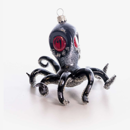 A black and silver glitter octopus Christmas ornament with red eyes, shown on a plain white background.