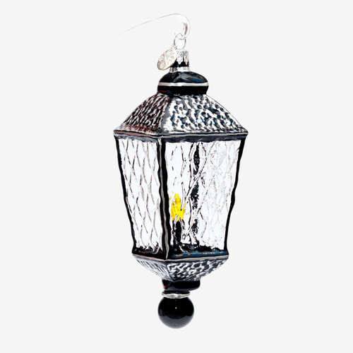 A hanging lantern ornament with a black metal frame, textured clear glass panels, a small yellow light inside, and a silver hanging loop on a plain light gray background.