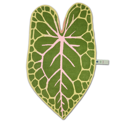 A heart-shaped rug designed to look like a green alocasia leaf, featuring a light green border, dark green textured sections, and a pink central vein pattern, shown on a plain white background with a small brand tag on the side.