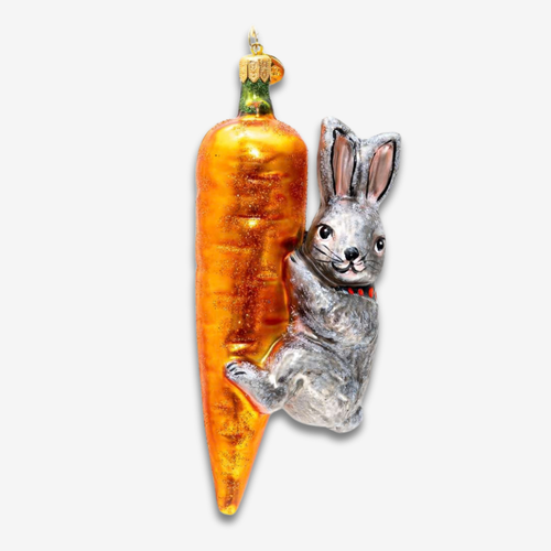 A decorative Christmas ornament featuring a silver rabbit clinging to a large orange carrot with a green stem, shown on a plain light gray background.