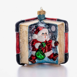 A hand-painted glass Christmas ornament shaped like an open book, featuring Santa Claus sitting inside and holding a green sack. The ornament has a gold hanging loop at the top and is photographed on a clean white background.