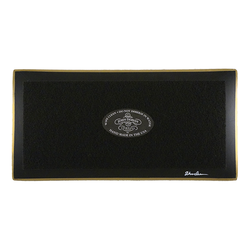 The back of a four and a half inch by nine inch tray that is painted black, with back felt, a gold trim and the John Derian Company logo sticker, signed by John Derian. 
