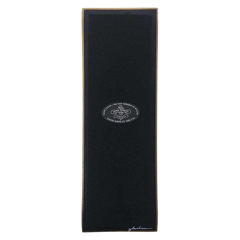 The back of a four and a half inch by nine inch tray that is painted black, with back felt, a gold trim and the John Derian Company logo sticker, signed by John Derian. 