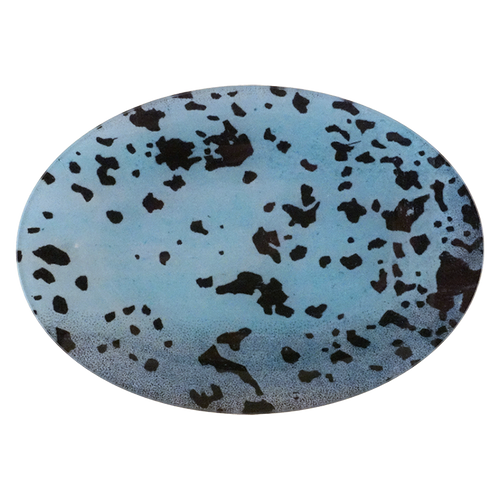 An oval-shaped decorative tile or coaster featuring a light blue background with a scattered pattern of dark brown and black organic spots, shown against a plain white background.