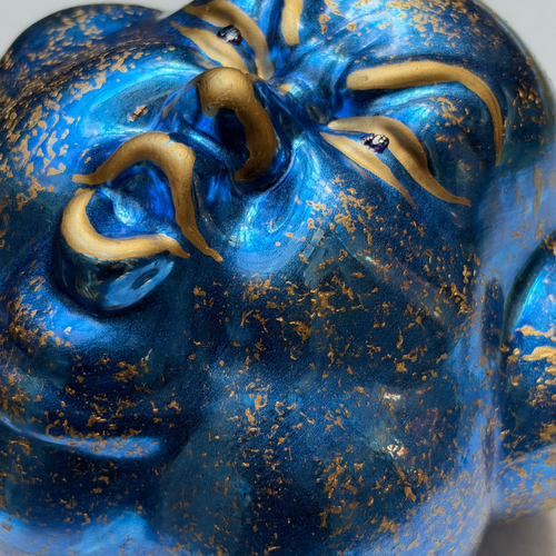 Blue cloud-shaped ornament with gold features and face on white background