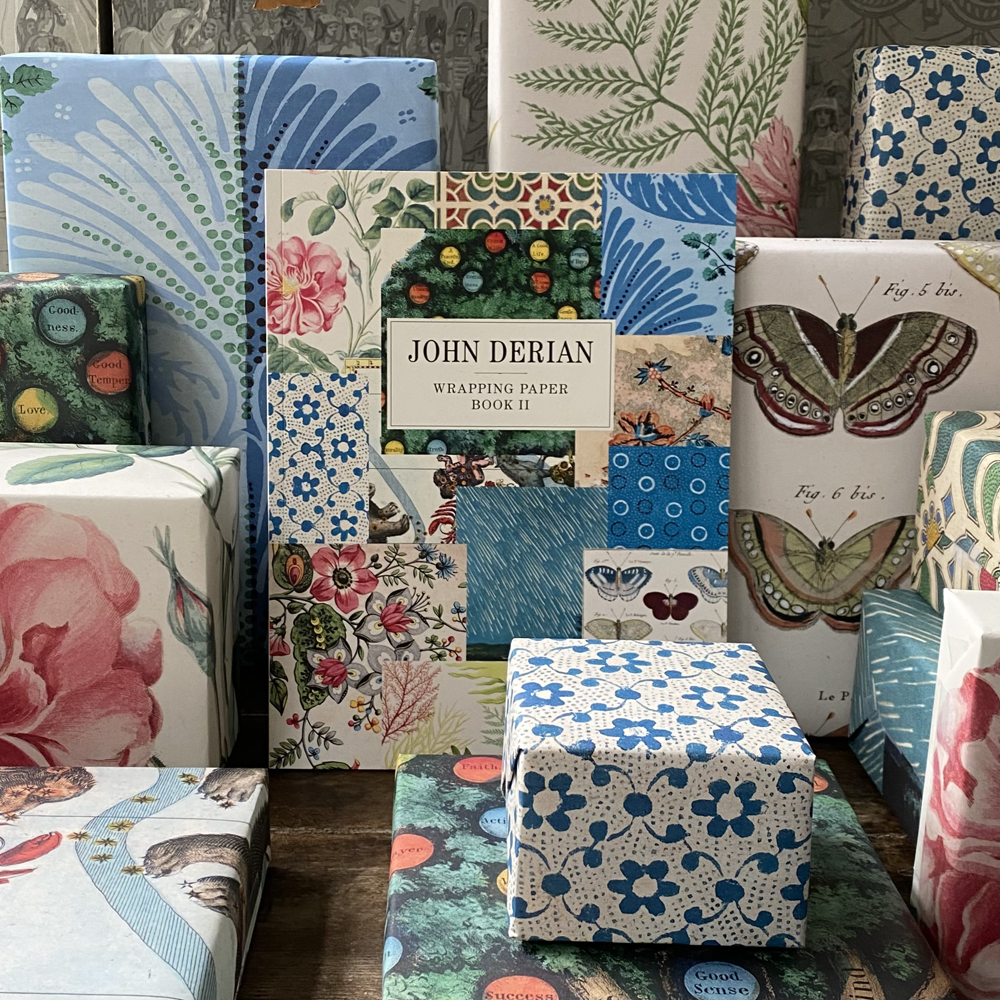 A collection of John Derian wrapping paper designs displayed on boxes and wrapped gifts, featuring botanical, butterfly, floral, and patchwork patterns.