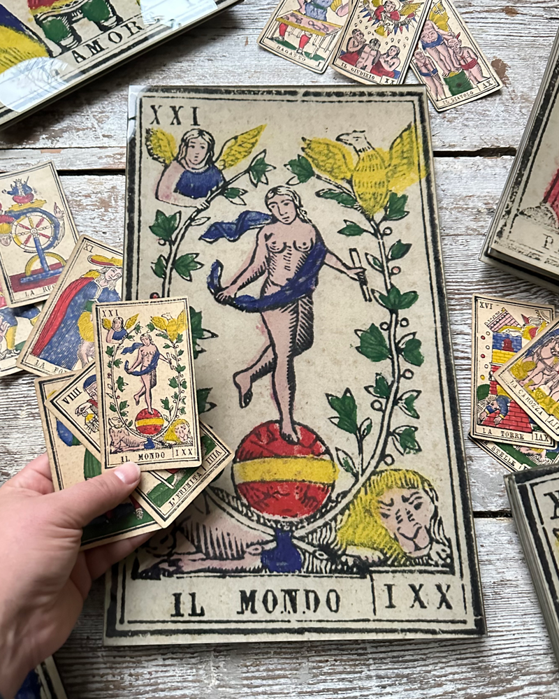 Tarot card with 'Il Mondo' (The World) and other cards on a wooden surface