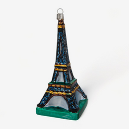 A small Eiffel Tower ornament with a dark blue and black body, gold accents, and a green base, shown on a plain light gray background.