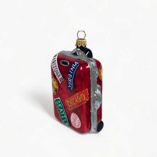A miniature red suitcase Christmas ornament decorated with travel stickers and a gold hanging loop, shown on a clean white background.