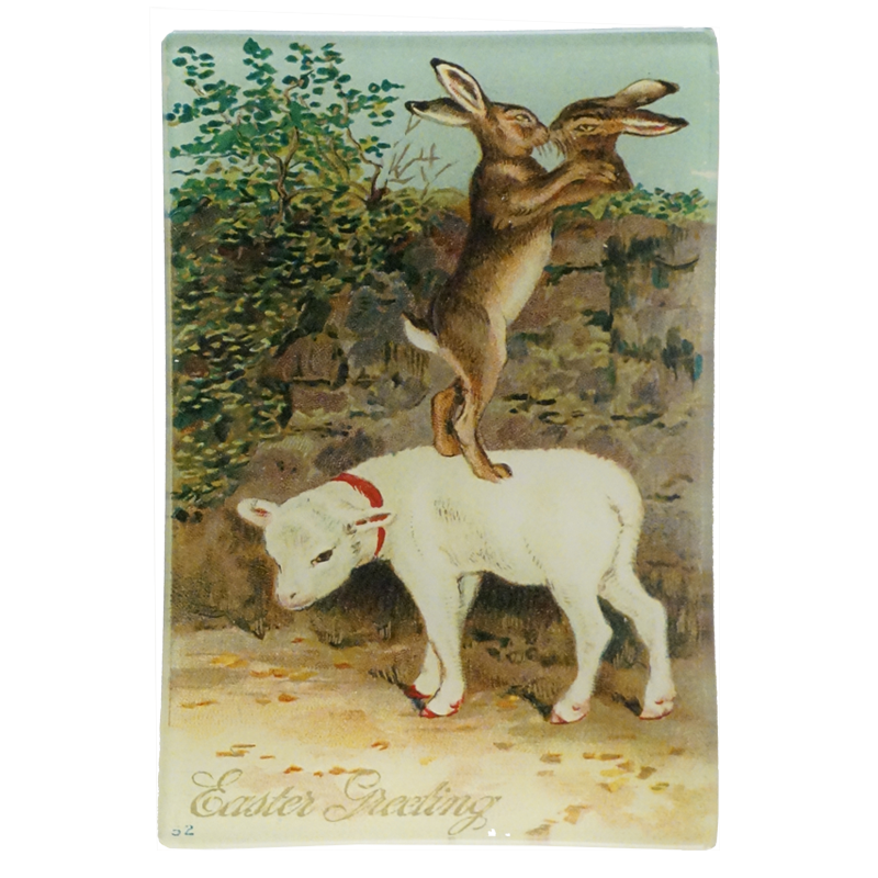 An illustration of two rabbits kissing standing on a lamb and Easter greetings text on a four and a half inch by six and a half inch glass tray. 