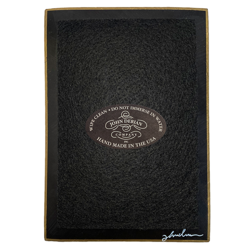 The back of a four and a half inch by six and a half inch tray that is painted black, with back felt, a gold trim and the John Derian Company logo sticker, signed by John Derian. 