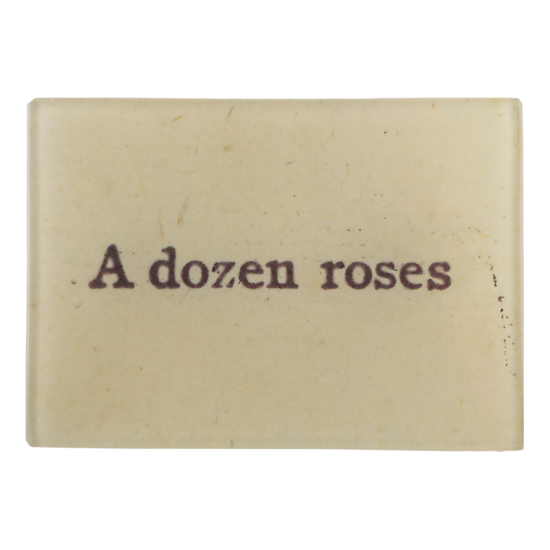 The text 'A dozen roses' written on a beige background on a three and a half inch by five inch glass tray.